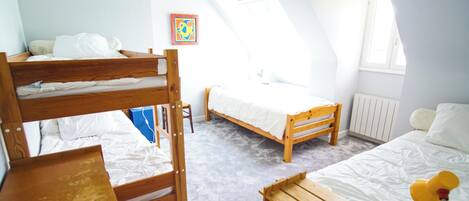 A dorm-style room with bunk beds, a single bed, a desk, and a radiator.