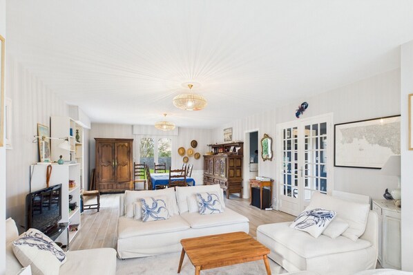 A spacious living room with a white sofa set, a wooden coffee table, and a dining area with a table and chairs.