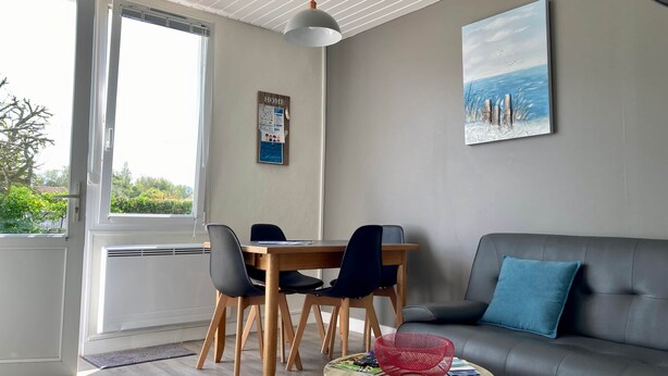 A modern living room with a dining area, a grey sofa, a table with chairs, a red basket, and a painting of a beach scene. - La Tranquille - House for 3 families (Saint-Denis-d'Oléron)