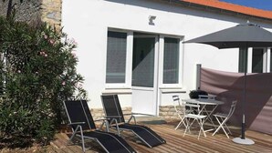 A patio with a wooden deck, a table with chairs, and a large umbrella. - La Tranquille - House for 3 families (Saint-Denis-d'Oléron)