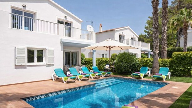 Eine zweistöckige weiße Villa mit Swimmingpool, Sitzgelegenheiten im Freien und Palmen.