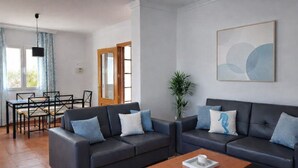 Ein modernes Wohnzimmer mit zwei dunklen Sofas, einem Holztisch und einem Essbereich mit Tisch und Stühlen.
