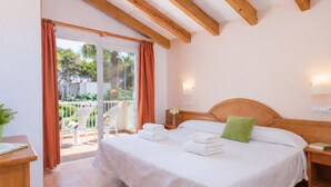 Ein Schlafzimmer mit Holzboden, einem Bett mit weißer Bettwäsche, einem grünen Kissen und einem Balkon mit orangenen Vorhängen.