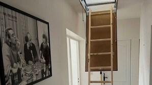A room with a wooden ladder leading to a loft space, a framed black and white photo on the wall, and a white door in the background. - Pretty Provencal house in a medieval village (Bouchet)