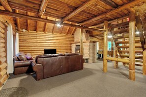 A log cabin interior with a leather sofa, a fireplace, and a wooden staircase. - Log Cabin Near Mount Rainier, Sleeps 8, Fireplace and Fire Pit (Ashford)