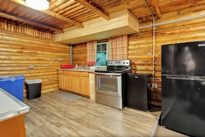 A log cabin kitchen with wooden walls, a stove, a refrigerator, and a sink.