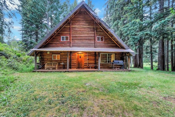 A log cabin with a porch, a chimney, and a small deck area.