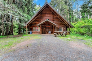 A log cabin with a pitched roof, a front porch with a bench, and a gravel driveway. - Log Cabin Near Mount Rainier, Sleeps 8, Fireplace and Fire Pit (Ashford)