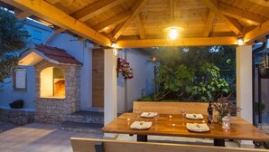 Et udendørs spiseområde med et træbord dækket til to under en pergola med lys.