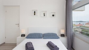 Et moderne hotelværelse med en seng, to puder, to sengeborde og havudsigt gennem et stort vindue.