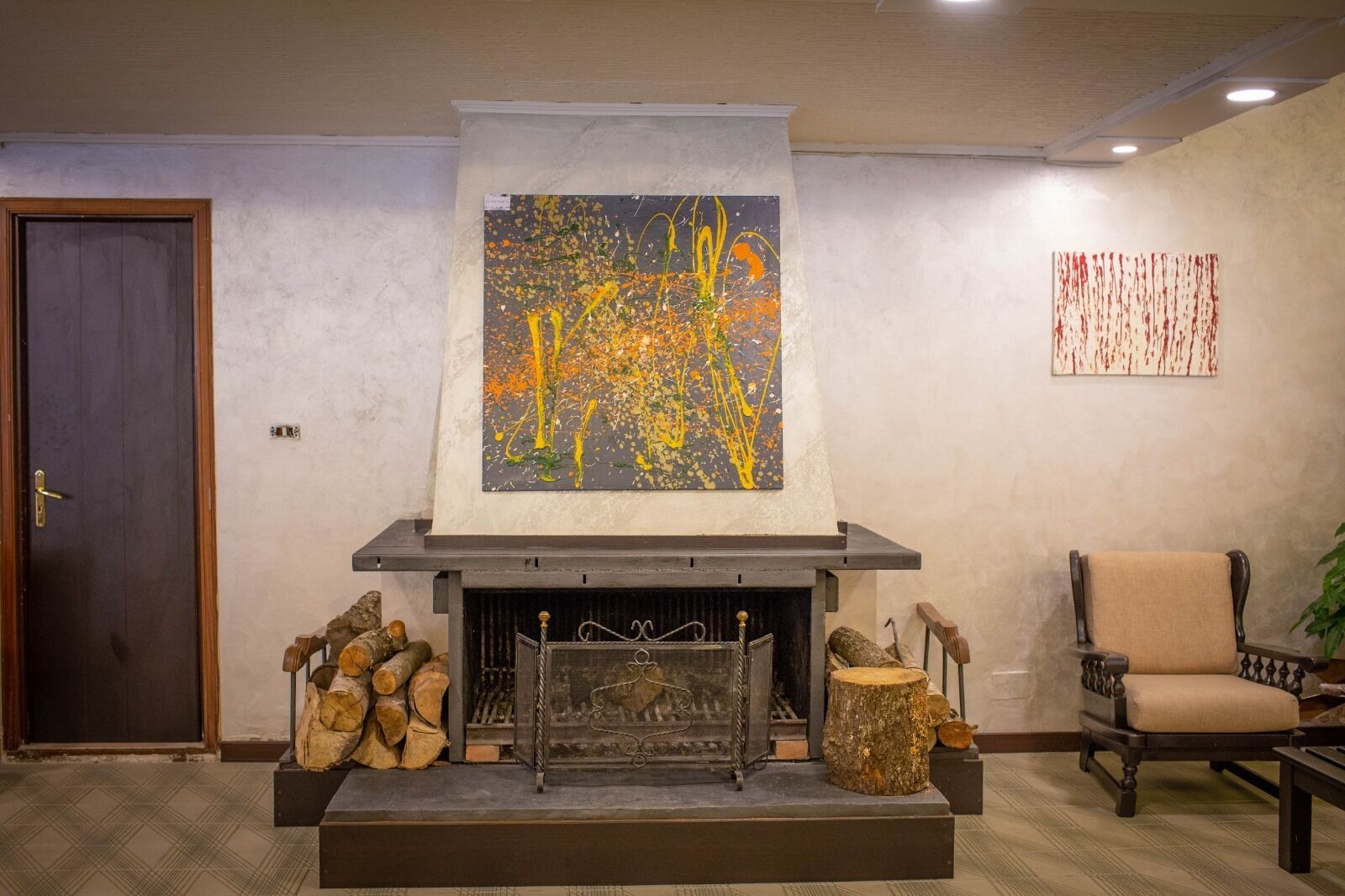 Una habitació amb una llar de foc, un quadre abstracte gran a la part superior i una cadira a la dreta.