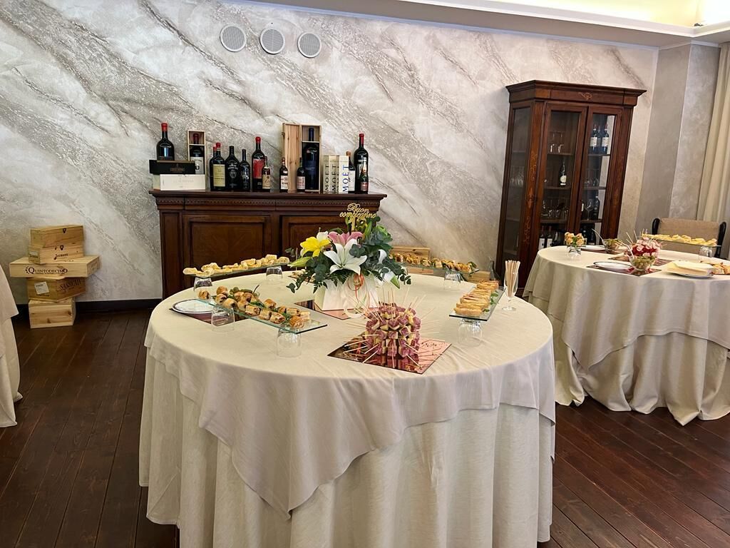 A room with a marble wall, a wooden cabinet with wine bottles, and a round table with food and drinks.