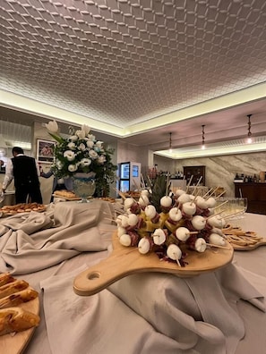 Une table de buffet proposant divers plats, notamment des brochettes de viande et de fromage, ainsi qu’un centre de table floral.