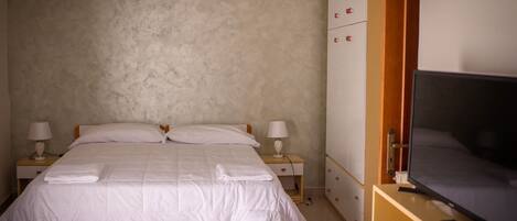 A bedroom with a bed, two bedside tables with lamps, a wardrobe, and a television.