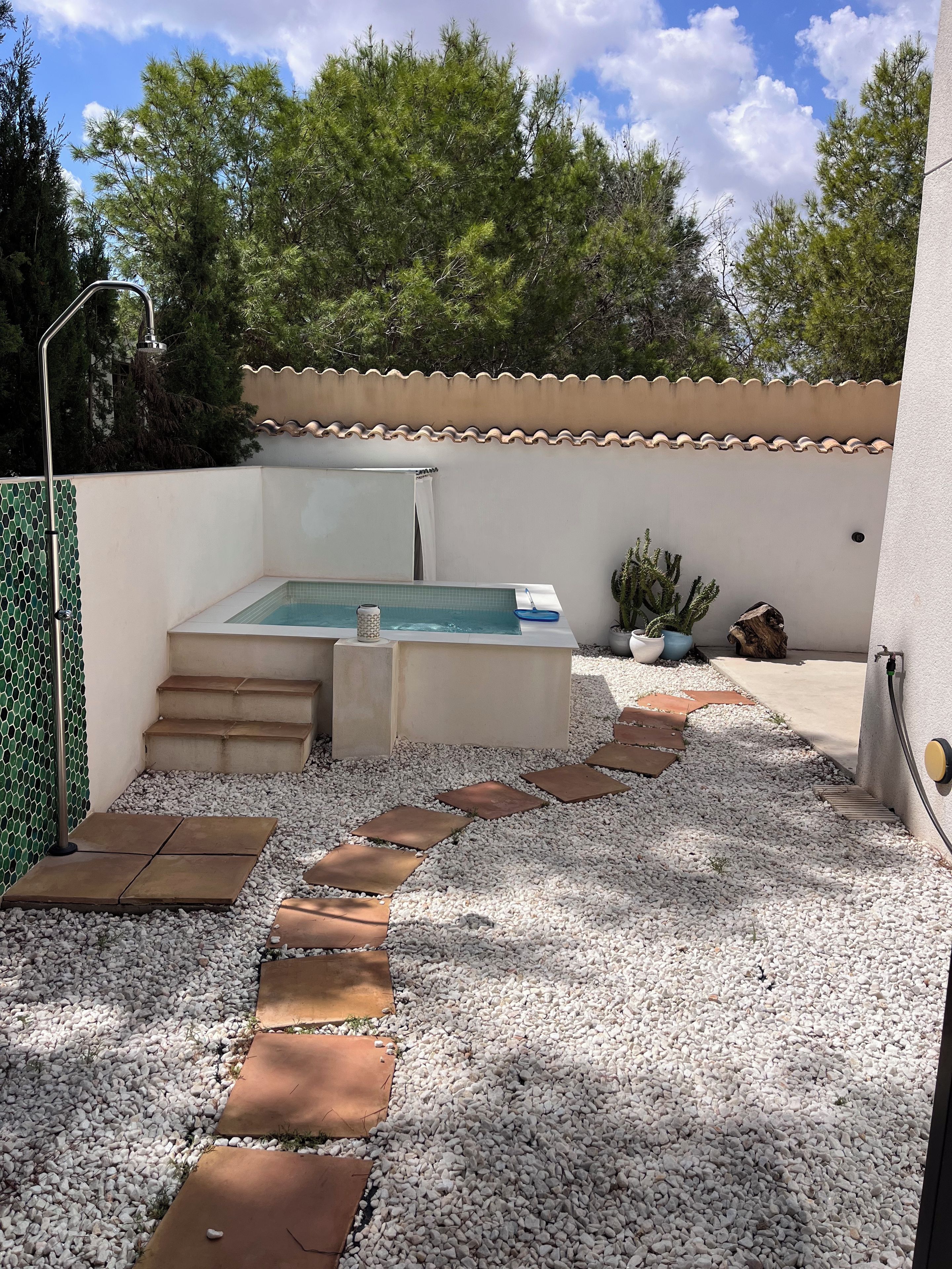 Una piscina con escalones que conducen a ella, rodeada de guijarros blancos y un sendero empinado.
