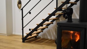 Una escalera de madera con barandillas negras que lleva a una habitación con estufa de leña.