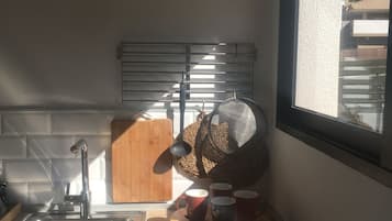 Een keuken met een raam, een spoelbak, een houten snijplank en een vergiet op het aanrecht.
