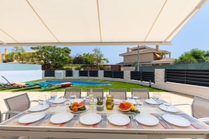 An outdoor dining area with a pool view, tables set with plates and cutlery, and a covered seating area.