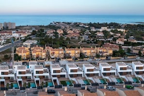 A coastal residential area with modern apartment buildings, a swimming pool complex, and a view of the sea.