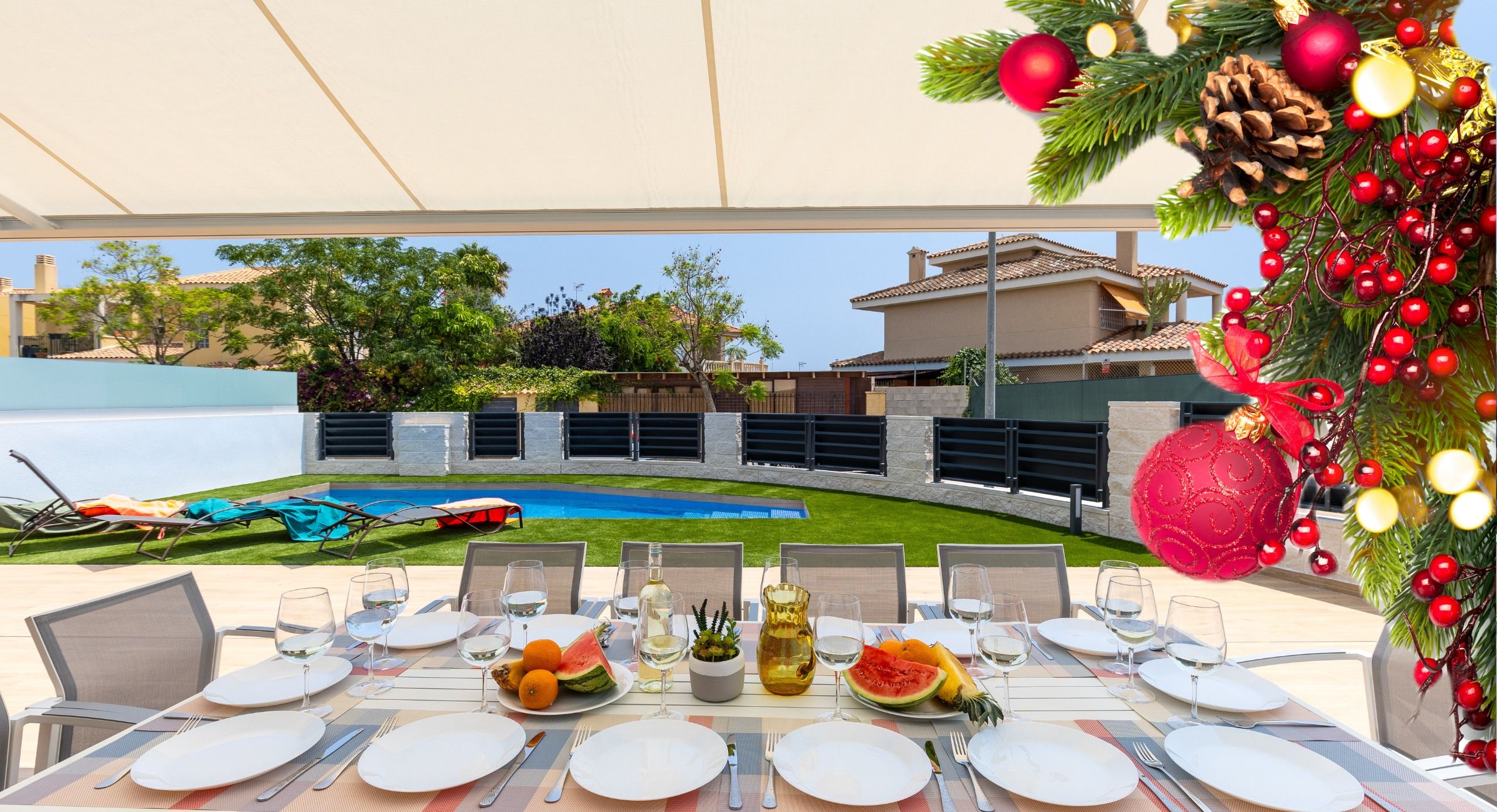 Ein Essbereich im Freien mit einem Pool im Hintergrund, ein Weihnachtsbaum mit Dekorationen und ein Tisch, der für eine Mahlzeit gedeckt ist.