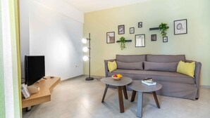Ein modernes Wohnzimmer mit einer Couch, zwei runden Tischen, einem Fernseher und Wandleuchten.