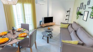 Ein modernes Wohnzimmer mit Essbereich, einer Couch, einem Fernseher und einem kleinen Tisch mit Obstschale.