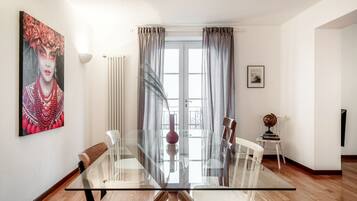 A modern dining area with a glass table, white chairs, and a view of the outdoors through large windows.