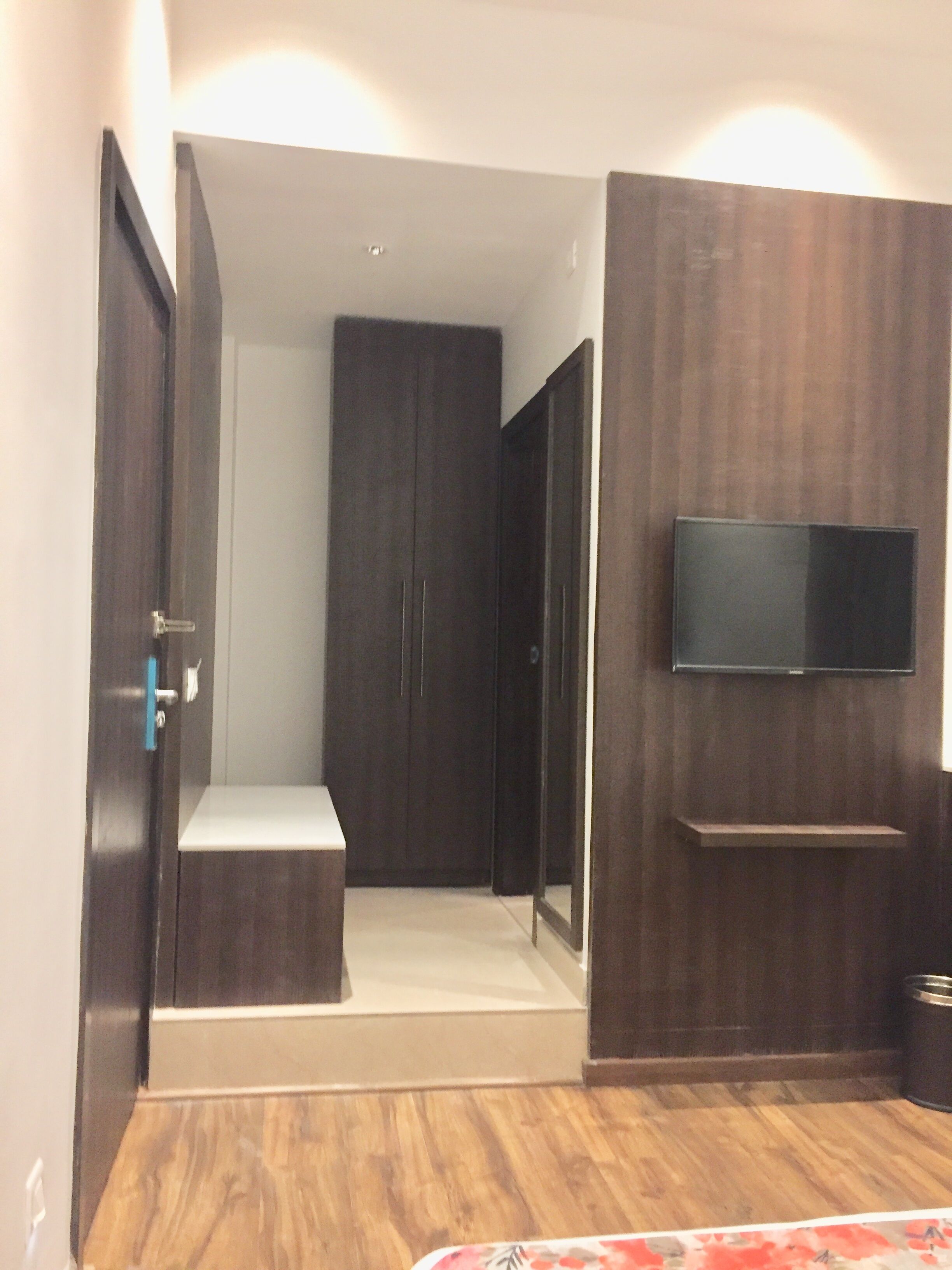 A modern bedroom with a built-in wardrobe, a TV mounted on the wall, and a bench at the entrance.