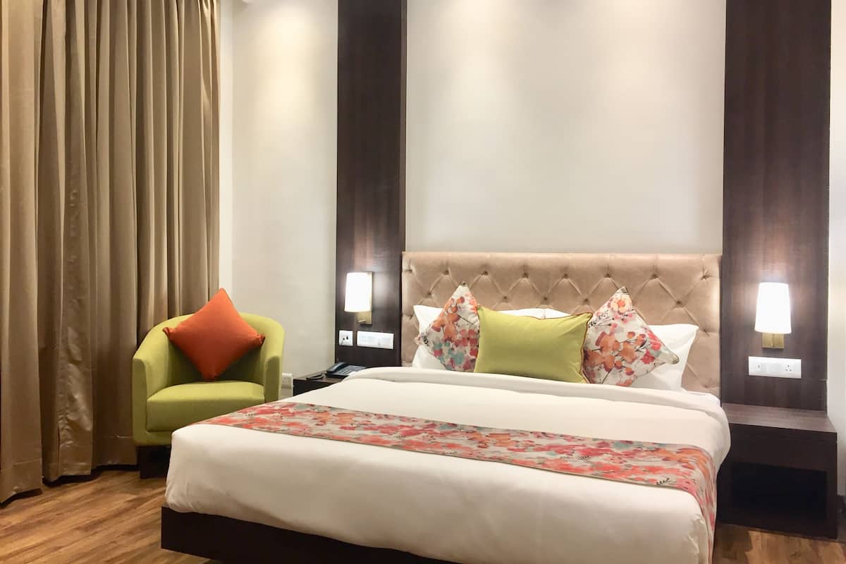 A hotel room with a large bed, a green armchair, and a window with curtains.