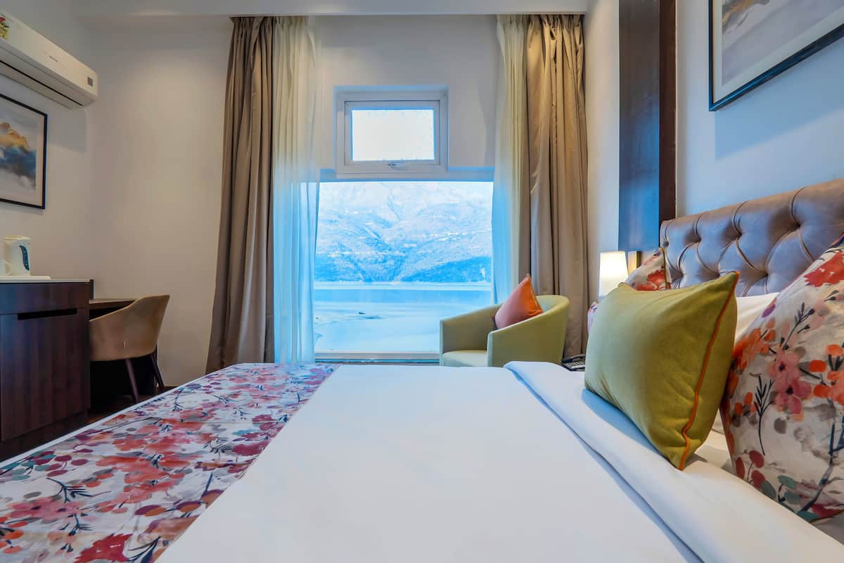 A hotel room with a bed, a desk, a chair, and a window with a view of a snowy landscape.