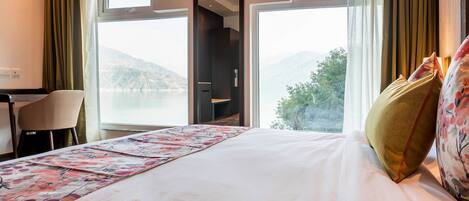 A hotel room with a bed, a desk, and a chair. There are two windows offering a view of the outdoors.