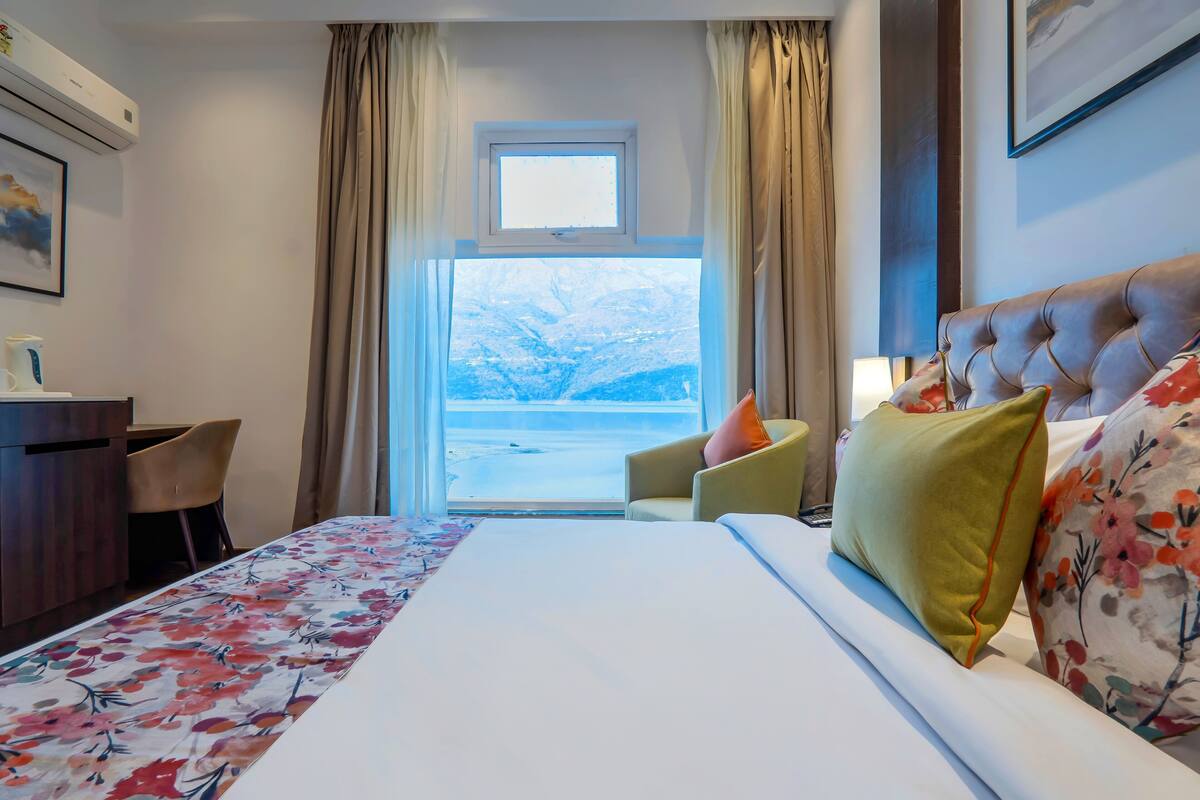 A hotel room with a bed, a desk, a chair, a window with curtains, and a view of a snowy landscape.