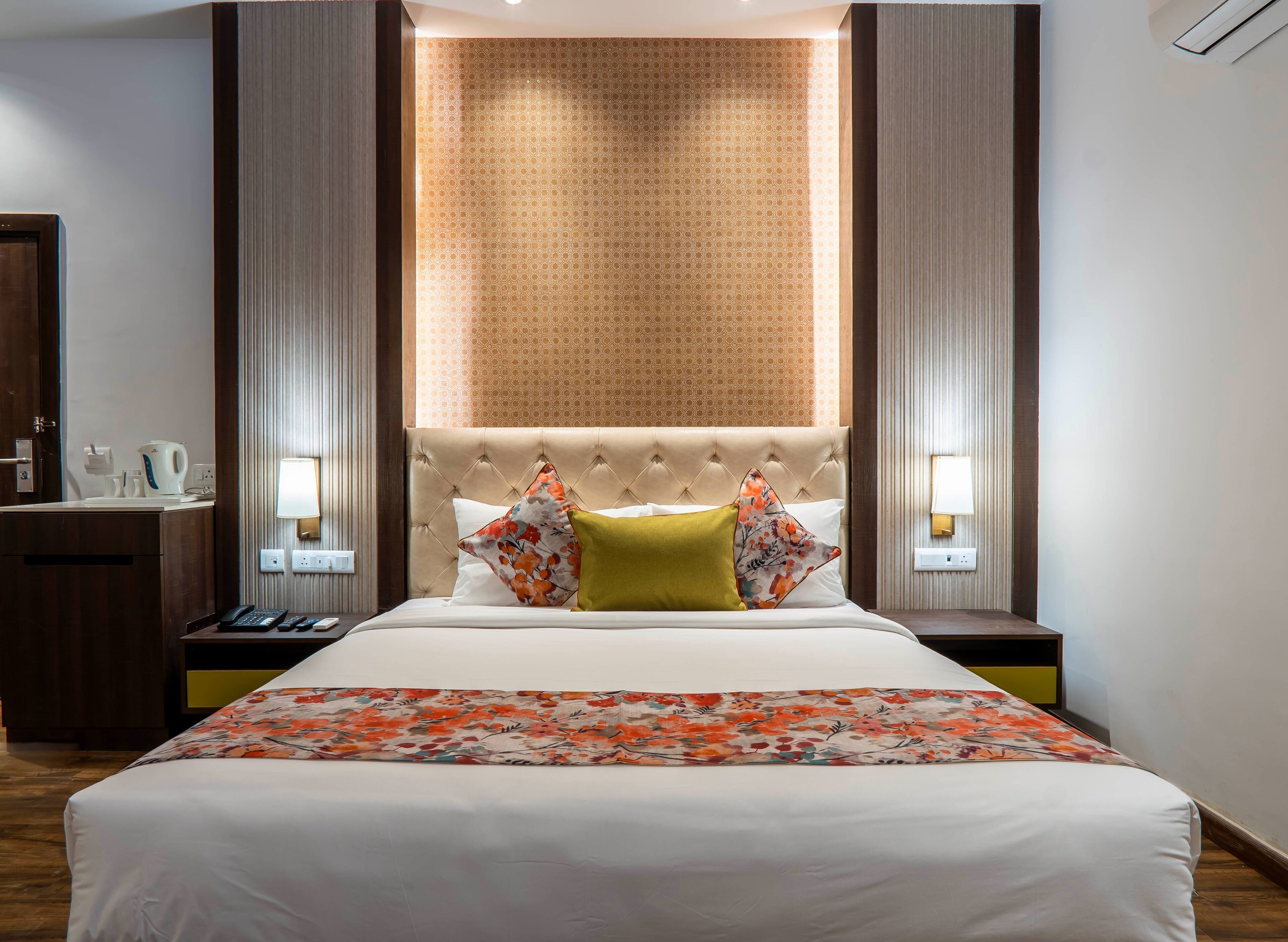A hotel room with a large bed, a nightstand, a mirror, a wall-mounted lamp, and a patterned wall.