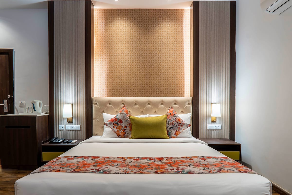 A hotel room with a large bed, a nightstand, a mirror, a wall-mounted lamp, and a patterned wall.