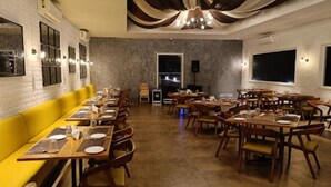 En restaurant med et langt, gult bænkeområde, træborde og stole.
