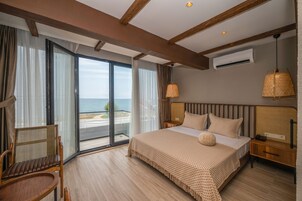 Habitación de hotel con una cama grande, una silla, una mesita de noche y vista al mar a través de una puerta corredera.