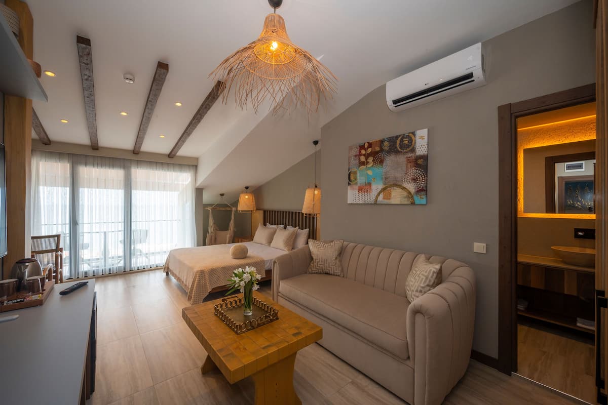 Une chambre d’hôtel moderne avec un grand lit, un canapé, une table basse en bois et un coin repas agrémenté d’un saladier.