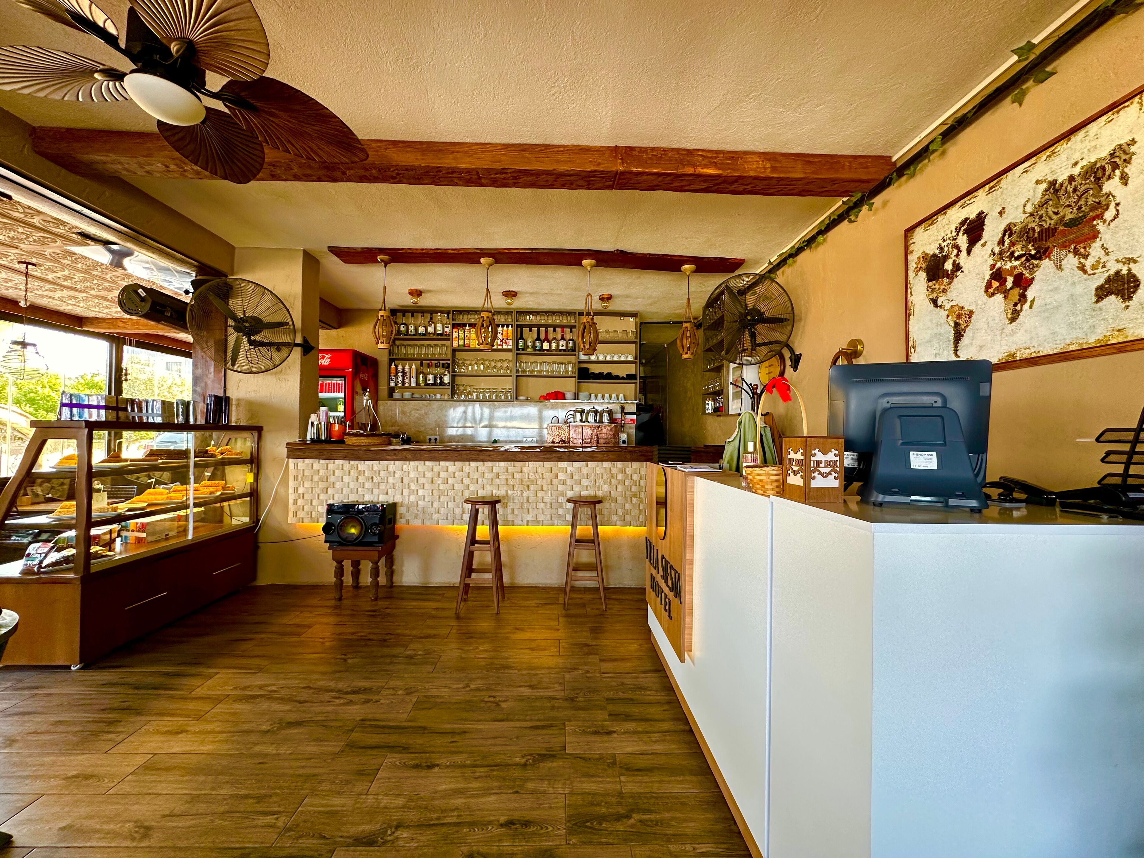 A bar area with wooden flooring, a counter with stools, a vintage fan, and a world map on the wall.