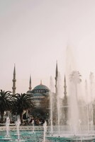 Una fuente con múltiples chorros de agua frente a una mezquita con cúpula y minaretes.