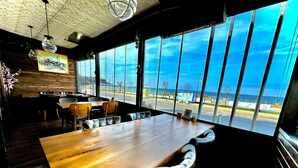 A restaurant with a large wooden table and chairs, a mural on the wall, and large windows offering a view of the beach and ocean. - Villa Siesta Hotel Istanbul Airport (Arnavutköy)
