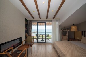 Habitación de hotel con balcón, cama, televisor y zona de estar con sillas y una mesa.