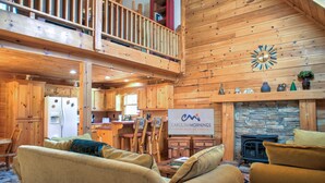 A spacious cabin interior with a dining area, kitchen, and a fireplace. - Pisgah Pines | Cozy Log Cabin w/ Hot Tub & Fire Pit Near Asheville Airport (Arden)