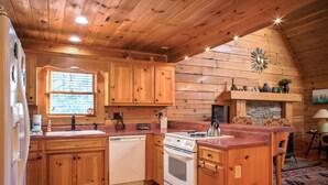 A wooden cabin interior with a kitchen featuring wooden cabinets, a stove, and a sink. - Pisgah Pines | Cozy Log Cabin w/ Hot Tub & Fire Pit Near Asheville Airport (Arden)