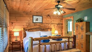 A wooden cabin-style bedroom with a bed, nightstands, and a ceiling fan. - Pisgah Pines | Cozy Log Cabin w/ Hot Tub & Fire Pit Near Asheville Airport (Arden)