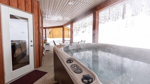 Una cabaña de madera con jacuzzi, una puerta y una ventana con vistas a un paisaje nevado.