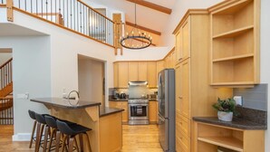 Una cocina moderna con armarios de madera, una isla central con taburetes de bar, un refrigerador de acero inoxidable y una lámpara de araña.