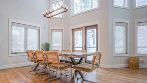 Un comedor espacioso con una mesa de madera y seis sillas, ventanas amplias y una lámpara colgante.