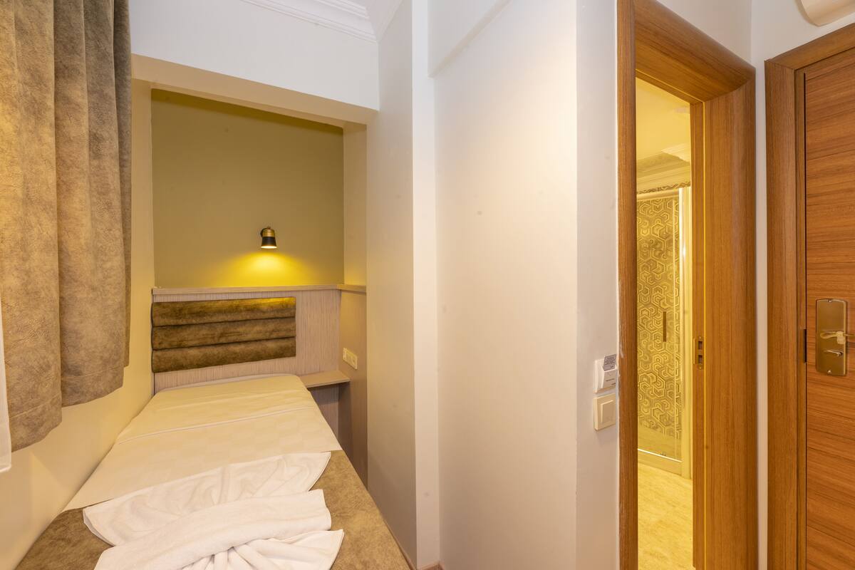 A hotel room with a bed, a bedside table, a lamp, and a wooden door.