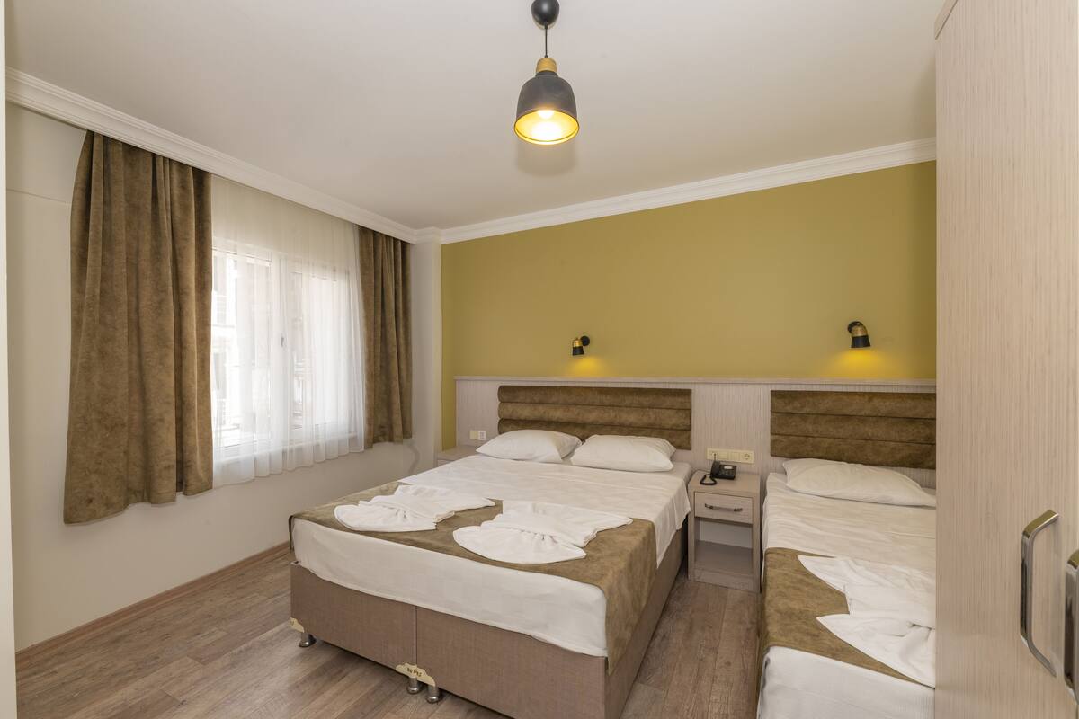 A hotel room with two beds, a bedside table, a lamp, and a window with curtains.