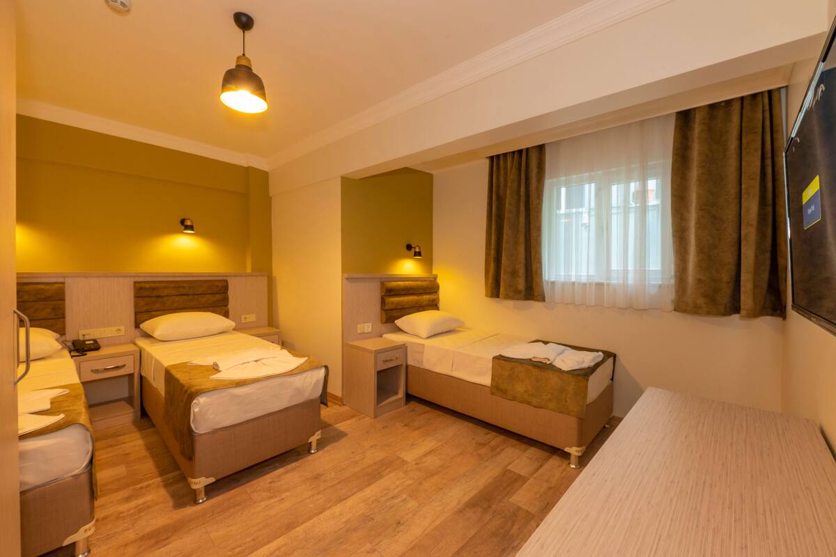 A hotel room with two beds, a desk, a chair, a TV, and a window with curtains.